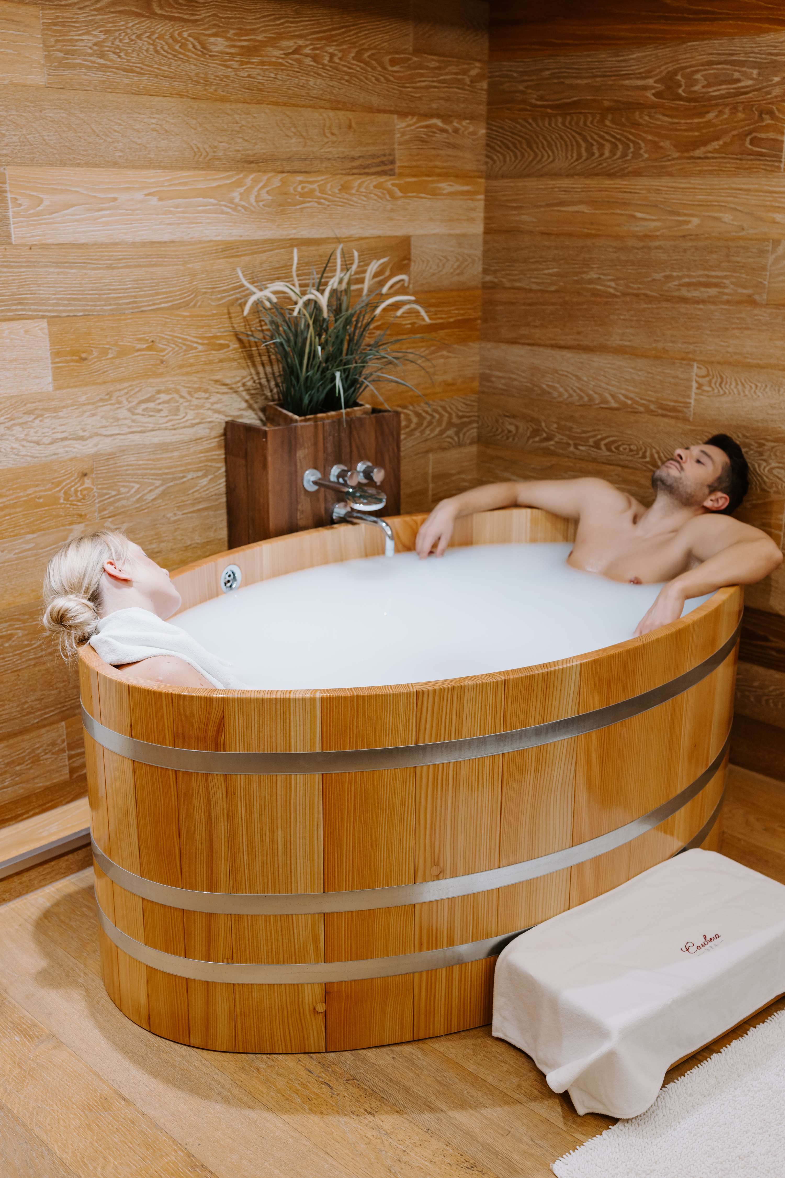 Couple in barrel-style wooden tub with natural wood panels