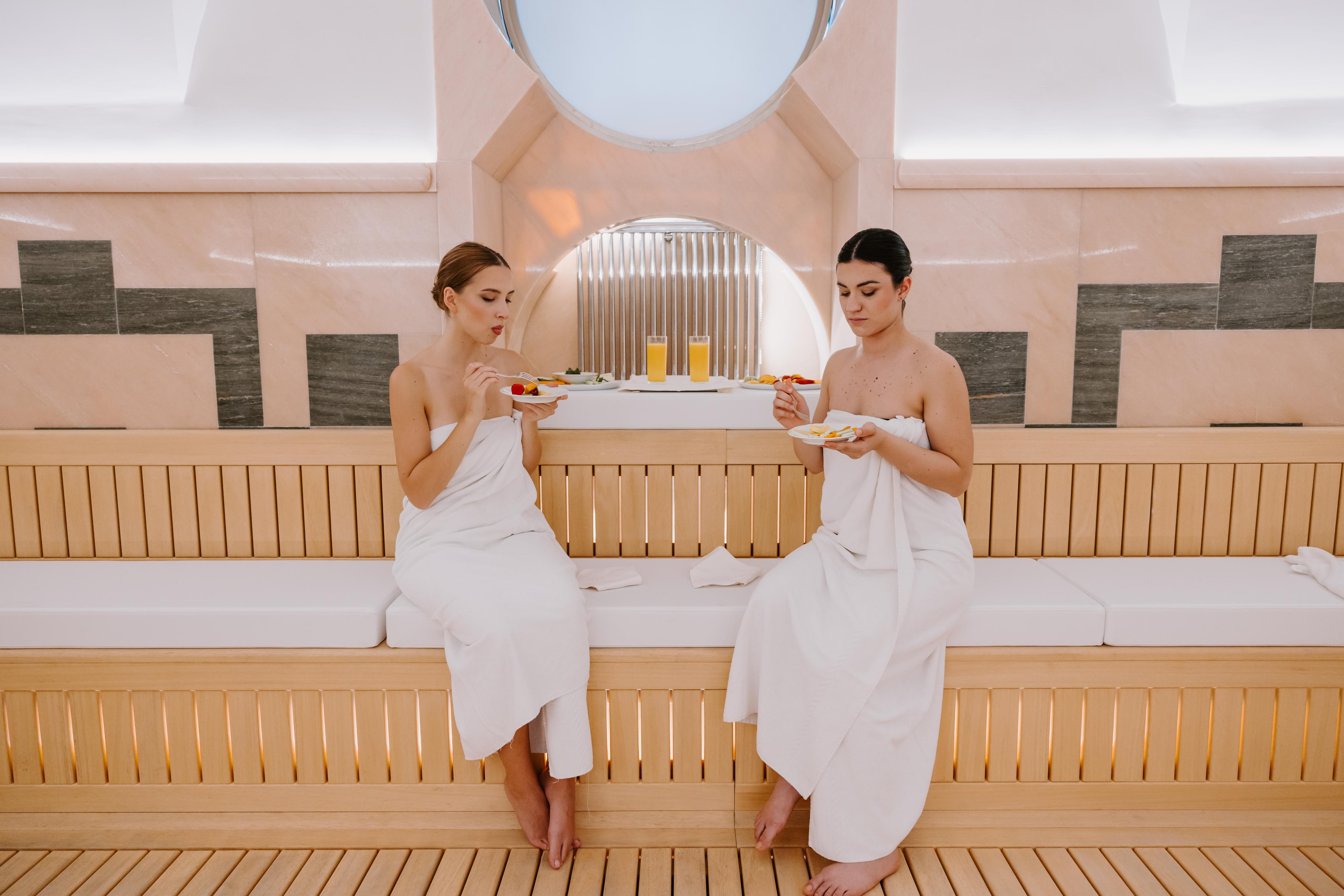 Two women in white towels enjoying snacks in relaxation area