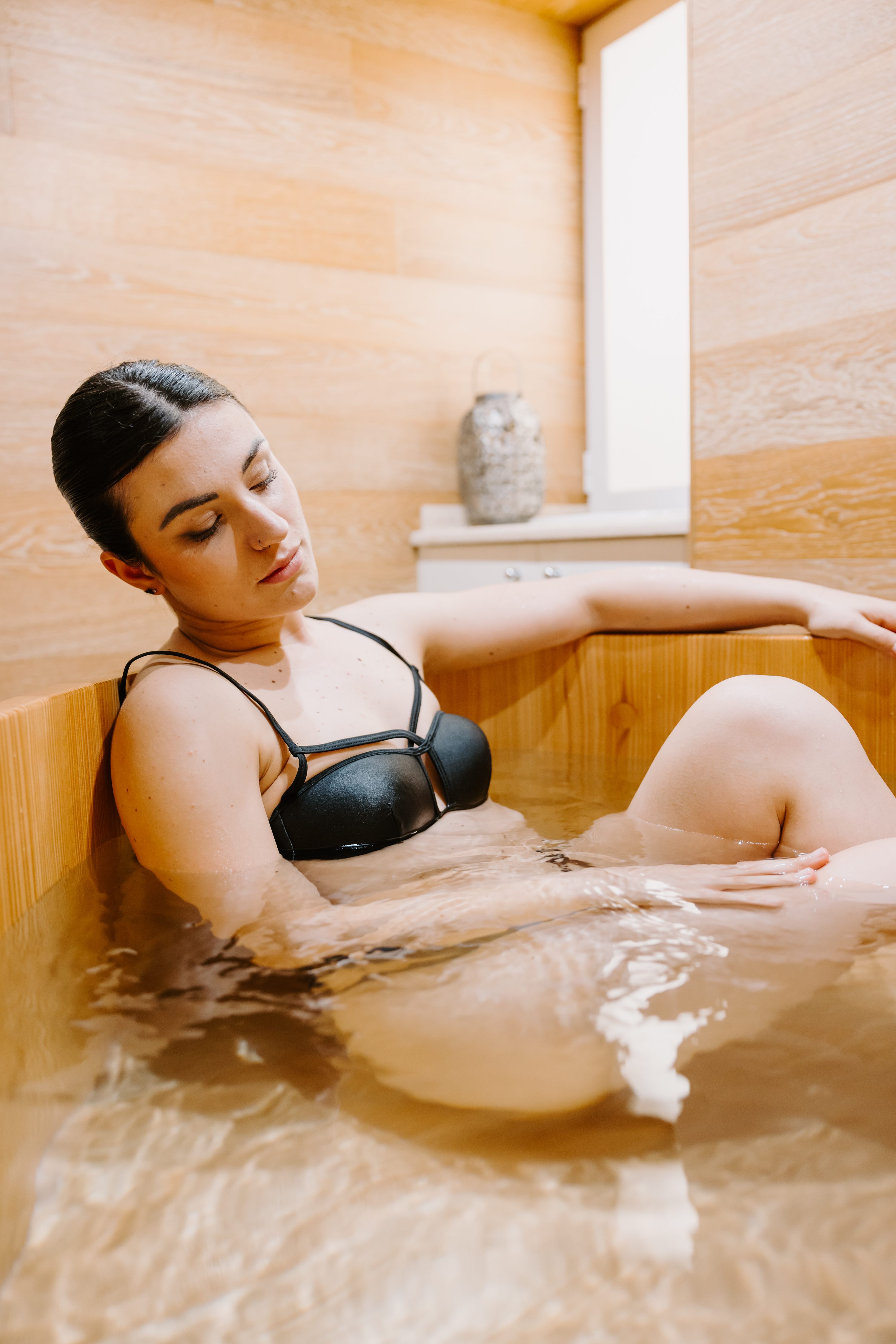 Woman relaxing in wooden tub with warm lighting
